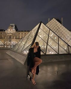 a woman leaning against a wall in front of a building with glass pyramids at night