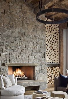 a living room filled with furniture and a fire place next to a stone wall covered in logs