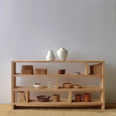 a wooden shelf with vases and bowls on it in front of a white wall