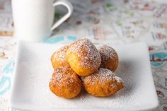 powdered sugar donuts on a plate with a cup of coffee in the background