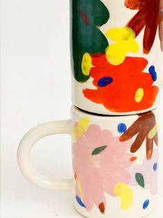 two coffee mugs with painted designs on them sitting next to each other in front of a white background