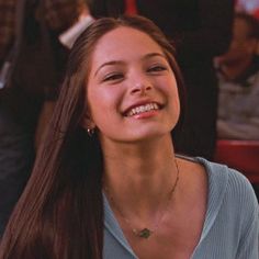 a woman with long hair smiling and wearing a blue shirt in front of other people