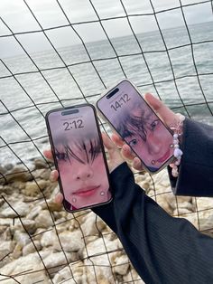 two people holding up cell phones in front of the ocean with their faces on them