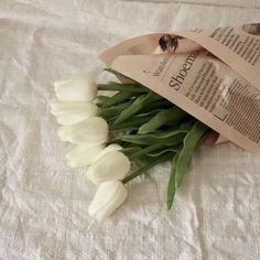 white tulips are wrapped in brown paper and placed on a bed sheet with an old book