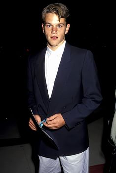 a young man in a suit and tie standing next to another person wearing white pants