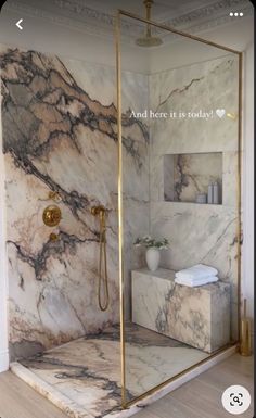 a bathroom with marble walls and flooring, gold fixtures and an open shower door