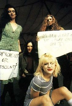 a group of young women holding signs in front of a tent with one woman sitting on the ground