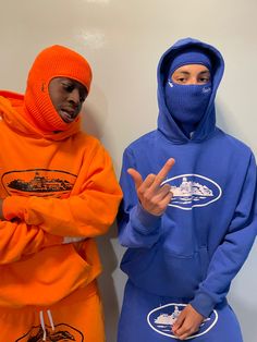 two people in orange and blue hoodies standing next to each other with their hands up