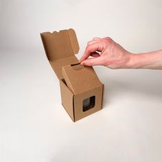 a hand is opening a cardboard box on a white surface, with the lid open