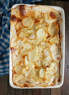 a casserole dish with potatoes in it on a blue and white towel next to a wooden table