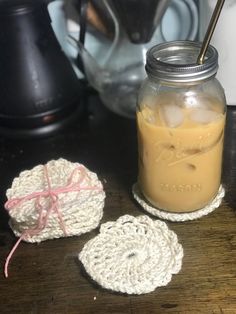 a mason jar filled with liquid next to two crocheted coasters