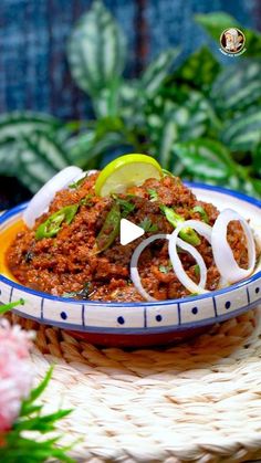 a bowl filled with chili and onions on top of a woven table cloth next to potted plants