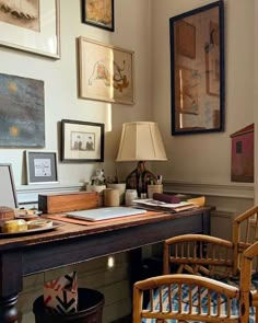 a desk with chairs and pictures on the wall above it, along with a lamp