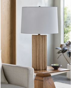 a table lamp sitting on top of a wooden table next to a white chair and window