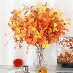 a vase filled with orange and yellow flowers next to a laptop