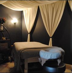 a massage room with black walls and white drapes on the ceiling, along with a round foot stool