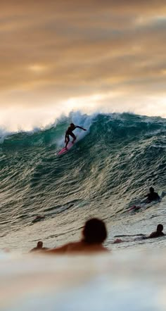 a man riding a surfboard on top of a wave in the ocean at sunset