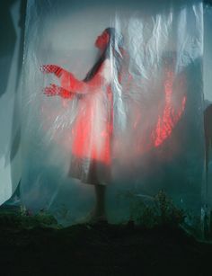 a woman standing in front of a white curtain with red light coming from her hands