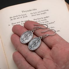 a pair of silver earrings sitting on top of an open book in someone's hand