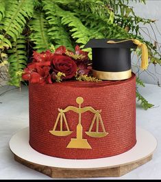 a graduation cake with a scale on top and flowers in the middle, surrounded by greenery