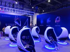 people are sitting in futuristic seats at an event with blue lighting on the walls and floor