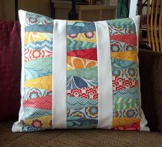 a colorful pillow on a brown couch with white ribbon around the back and side pockets