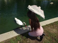 a woman kneeling down next to a white swan