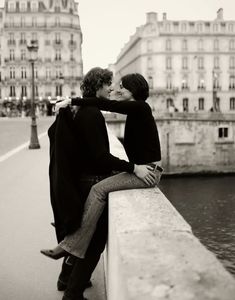 black and white photograph of two people kissing each other on a bridge over the water