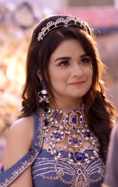 a woman in a blue dress with jewels on her neck and shoulder, smiling at the camera