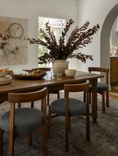 a dining room table with chairs and a vase filled with flowers sitting on top of it