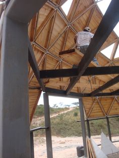 a man standing on top of a metal beam under a wooden roof in a building