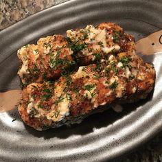 some meat patties with sauce and parsley on a metal plate next to a wooden spatula