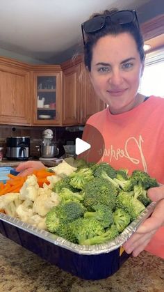 a woman holding a pan full of broccoli and carrots in the kitchen