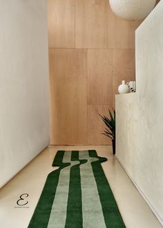 a green and white striped rug on the floor in front of a wall with a plant