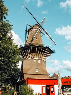 an old windmill sits in front of a red building on a sunny day with blue skies and white clouds