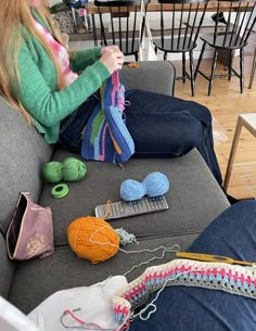 a woman sitting on top of a gray couch next to crochet and knitting supplies