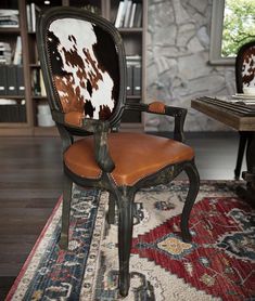 an old chair with cow hide on it in front of a table and bookshelf