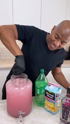 a man in black shirt standing next to pink liquid and other items on counter top