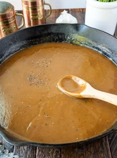 a wooden spoon is in a large skillet with some food on the table next to it