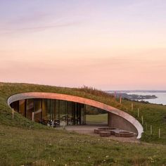 a curved building with grass on top and water in the backgroung at sunset