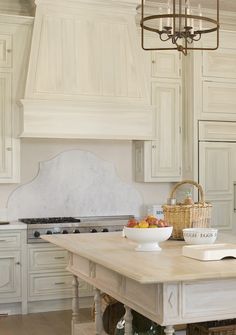 a white kitchen with an island and chandelier in the center, surrounded by wooden flooring