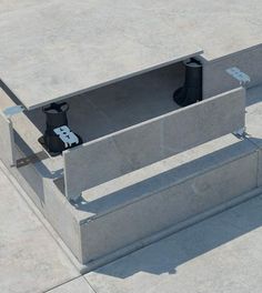 two black vases sitting on top of a cement box in the middle of a concrete floor