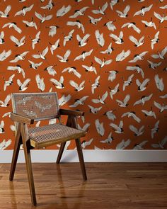 a chair sitting in front of an orange wall with white birds flying over it on it