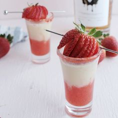 two cups with strawberries on the side and a bottle of booze in the background