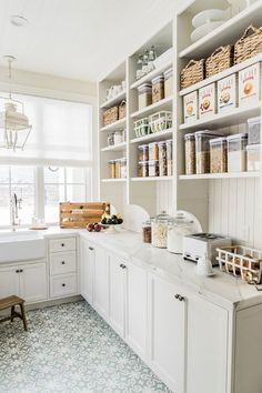 a kitchen with lots of white cabinets and shelves filled with food on top of them