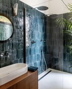 a bathroom with blue tiles and a large plant in the shower area, along with a white sink