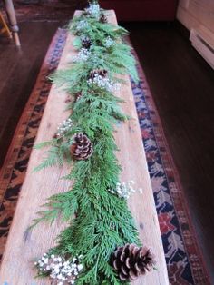 a long wooden table topped with pine cones and greenery next to a rug on the floor