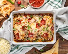 a casserole dish with tomatoes, cheese and sauce on a wooden table next to pita bread