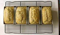 four loafs of banana bread sitting on a rack next to each other in front of a white wall