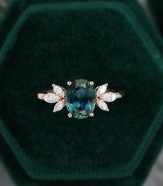 an emerald colored ring with two white diamonds on it in a green velvet jewelry box